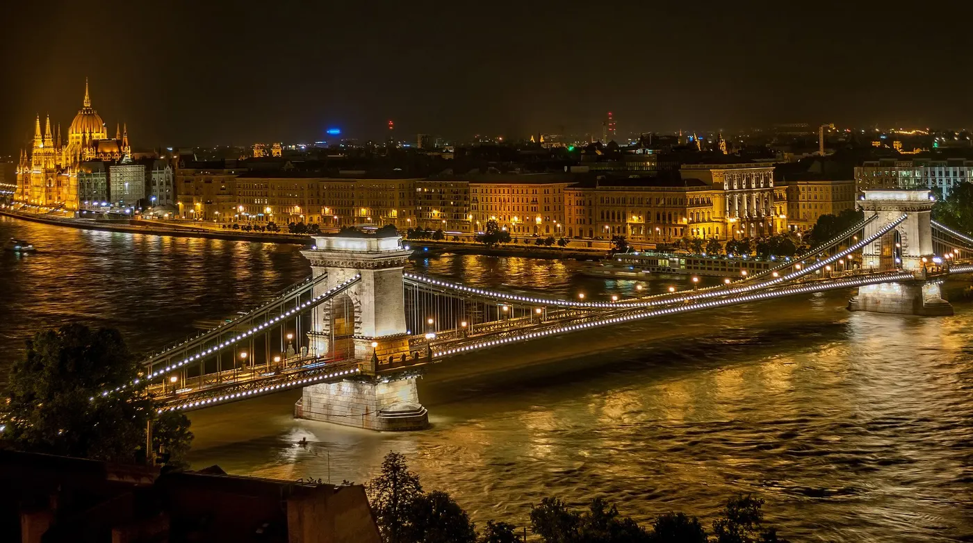 The Chain Bridge lit up at night over the Danube, with the Parliament on the Pest bank