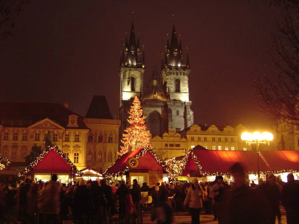 Christmas market stalls and a lit tree on Old Town Square, with the Týn Church behind