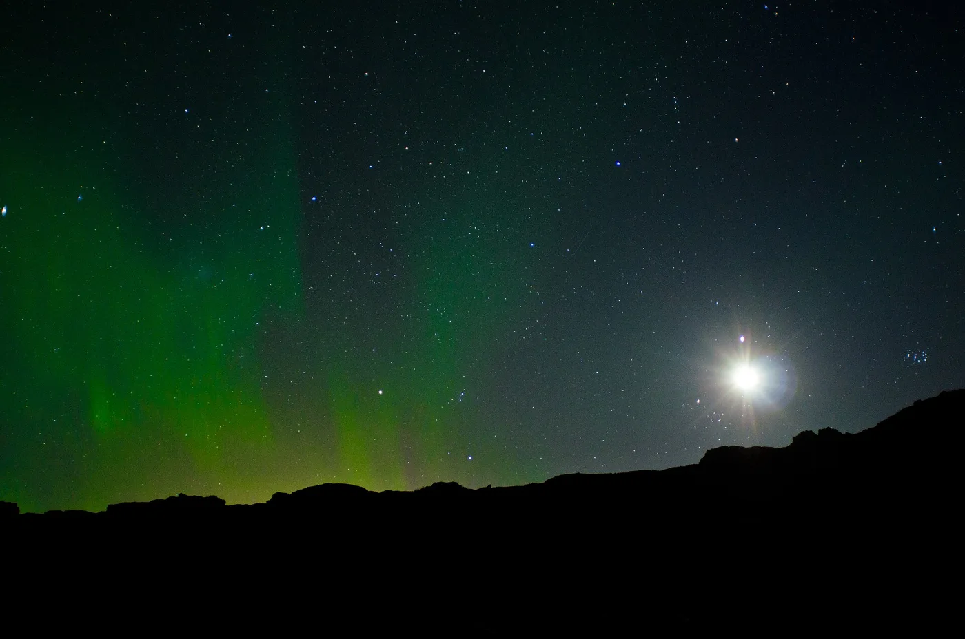 Green northern lights glowing above a dark Icelandic horizon